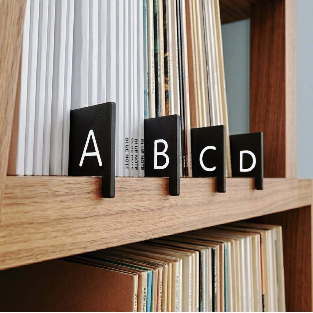 Alphabetical A-Z vinyl record dividers organize vinyl albums on a wooden shelf, and grab onto edge of shelf with a lip feature.