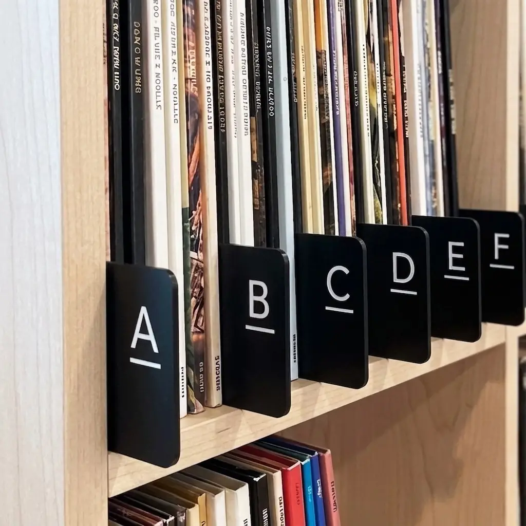 Organized vinyl record collection with black alphabetical divider tabs on a wooden shelf.