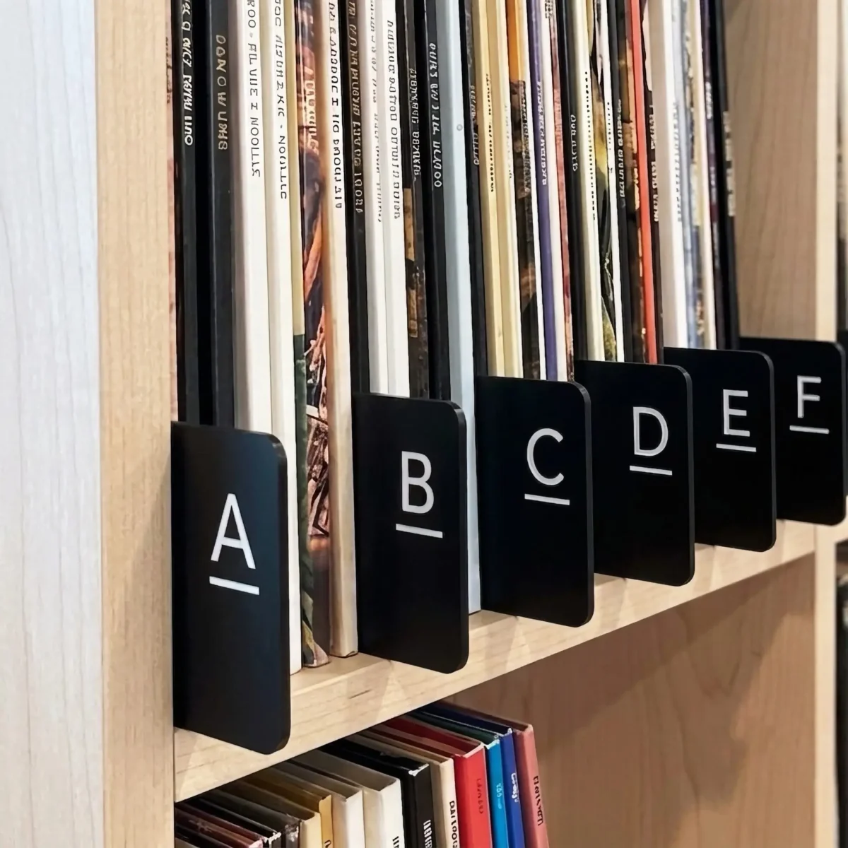 Alphabetically organized vinyl records on a light wooden shelf with black letter dividers.