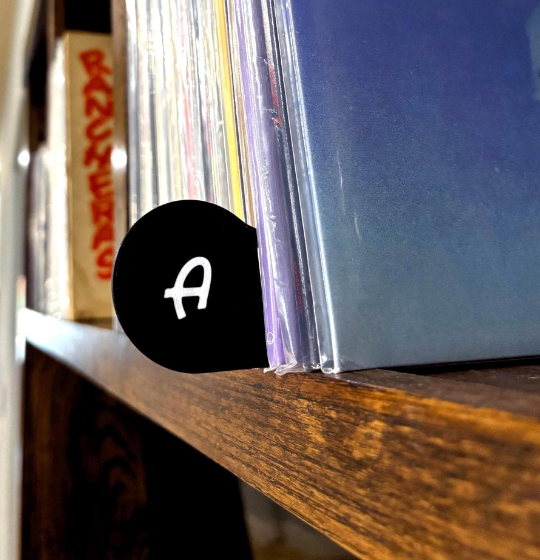 Black vinyl record divider tab with letter A organizing albums on a wooden shelf.