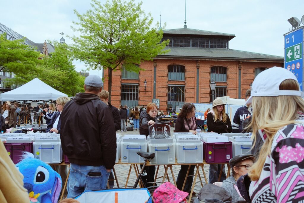 People browse vinyl records at an outdoor flea market in a historic public square.