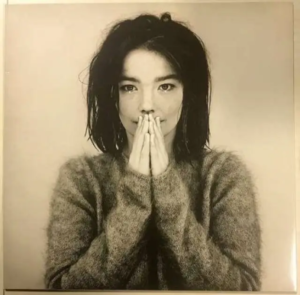Sepia portrait of singer Björk in a fuzzy knit sweater with hands pressed together.