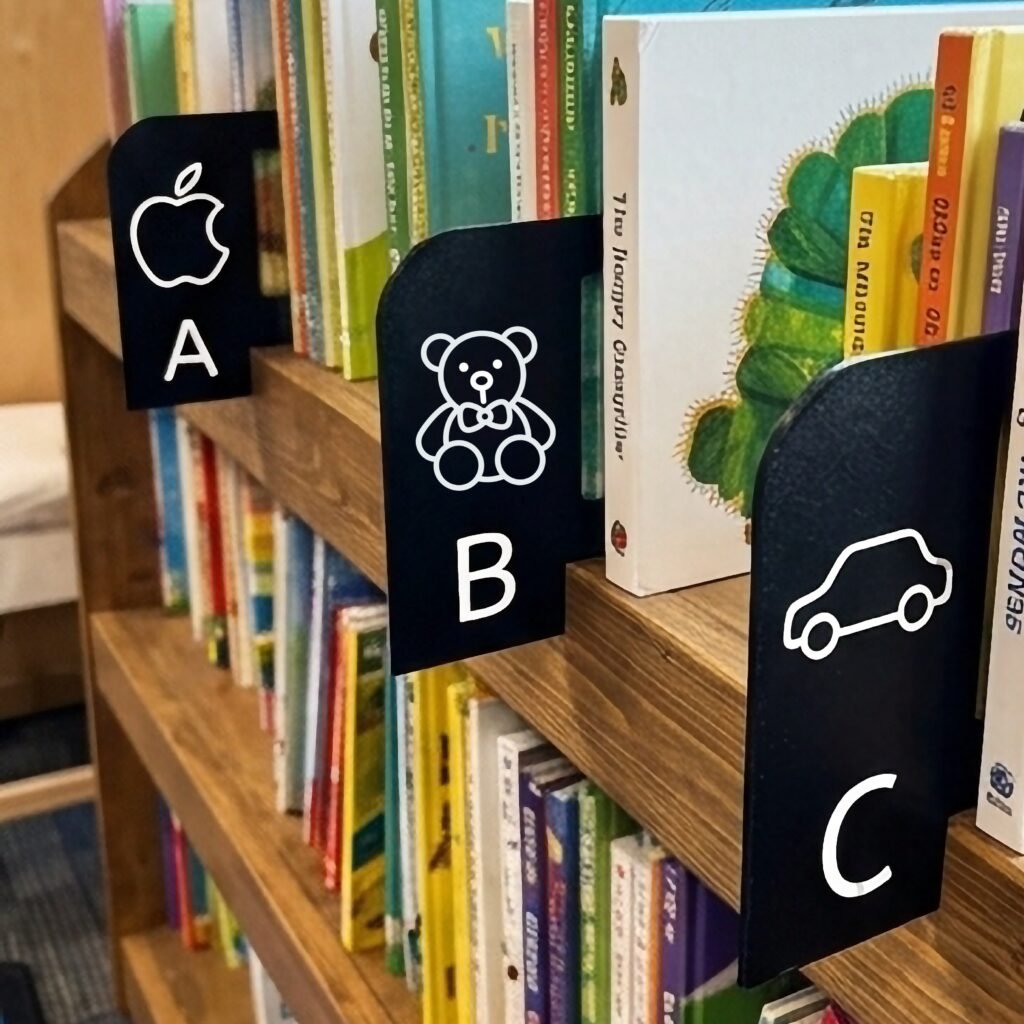 Wooden childrens bookshelf with custom black alphabet dividers organizing colorful books.