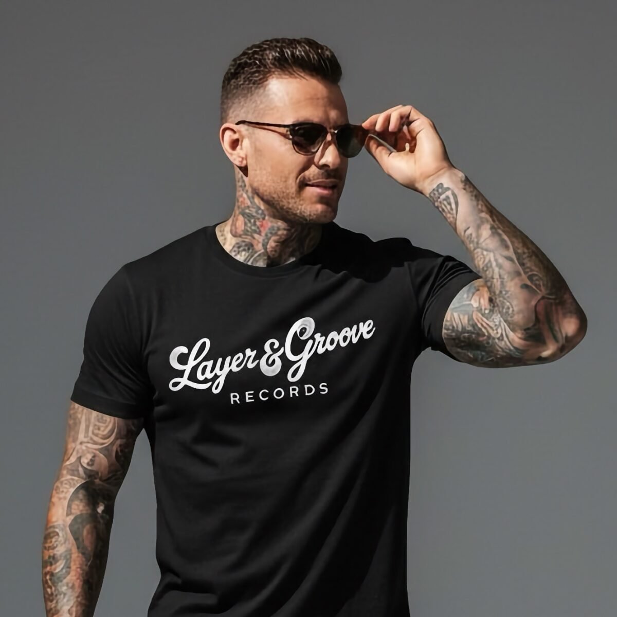 Tattooed man wearing sunglasses and a black Layer & Groove Records graphic t-shirt.