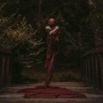Mysterious figure wrapped in a long red dress on a wooden forest bridge.