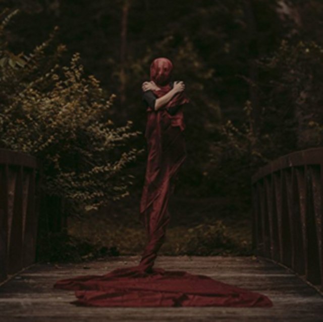 Mysterious figure wrapped in a long red dress on a wooden forest bridge.