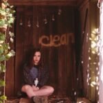 Young woman holding a spray paint can in front of a rustic wooden wall.