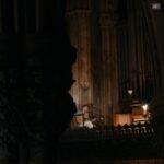 A guitarist playing an acoustic guitar in a grand, dimly lit cathedral.
