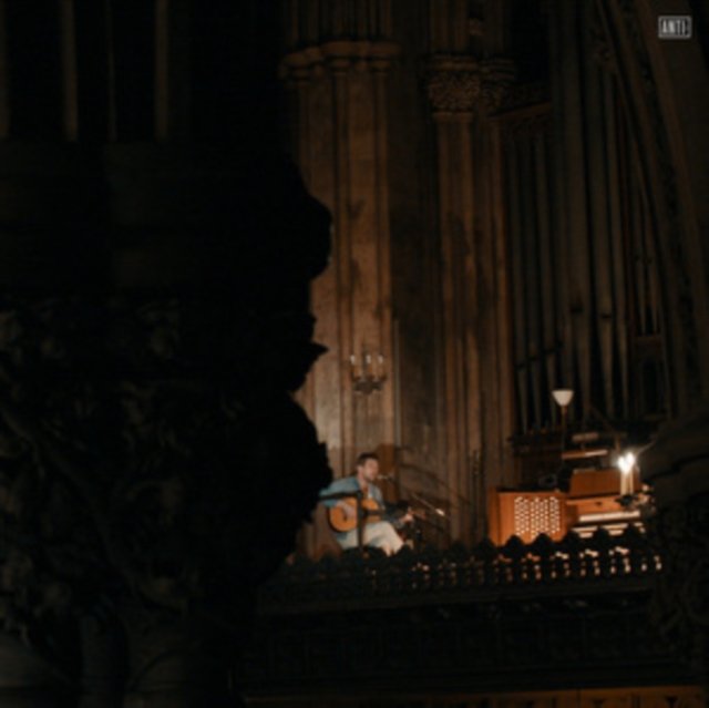 A guitarist playing an acoustic guitar in a grand, dimly lit cathedral.