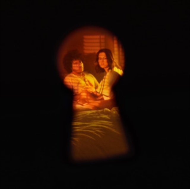 Keyhole view of a couple sitting on a bed in a warmly lit room.