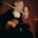 Artistic motion-blurred photo of a musician playing guitar and singing into a microphone.
