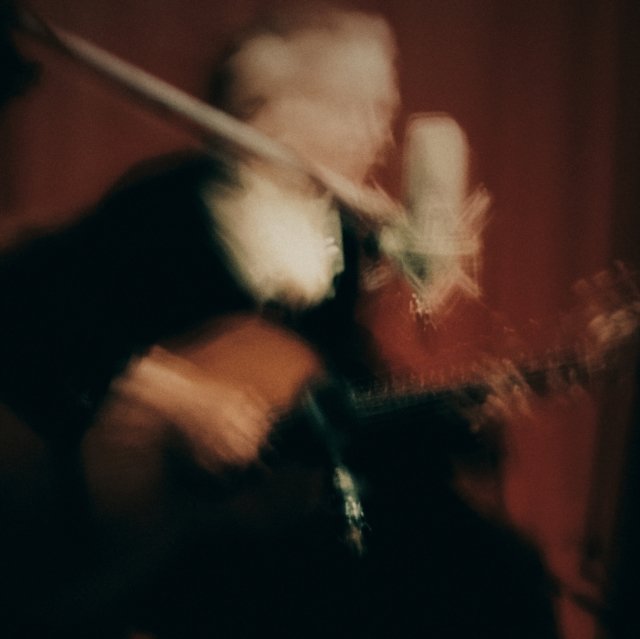 Artistic motion-blurred photo of a musician playing guitar and singing into a microphone.