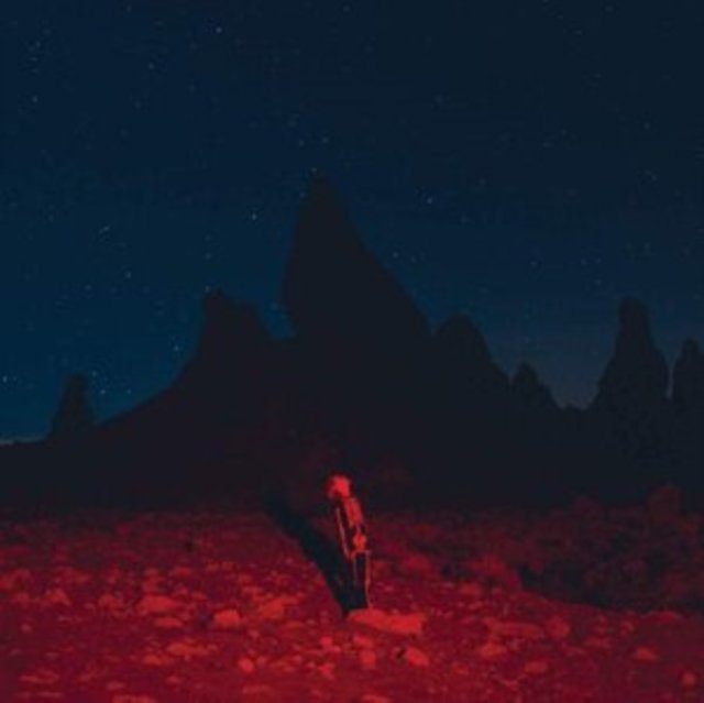 Person in a skeleton suit standing on a red-lit desert facing dark mountains.