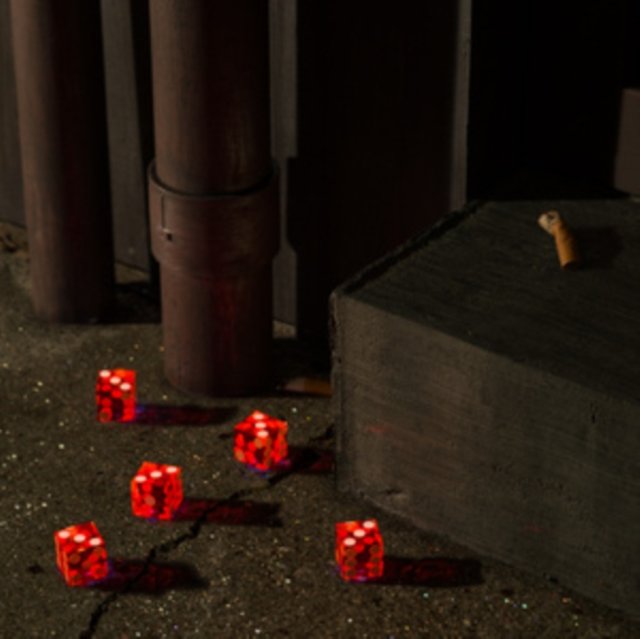 Five translucent red dice scattered on dark asphalt in a moody alleyway.