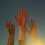 Three tattooed arms raised toward the sky in warm sunlight.