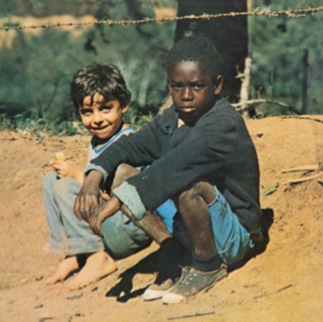 Two young boys sitting on a dusty dirt bank in a rural setting.